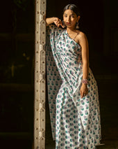 a woman in a white and green dress leaning against a pole