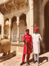 man in red robe standing near white concrete building during daytime