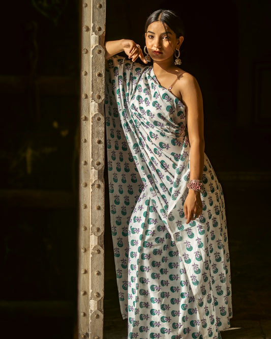 a woman in a white and green dress leaning against a pole