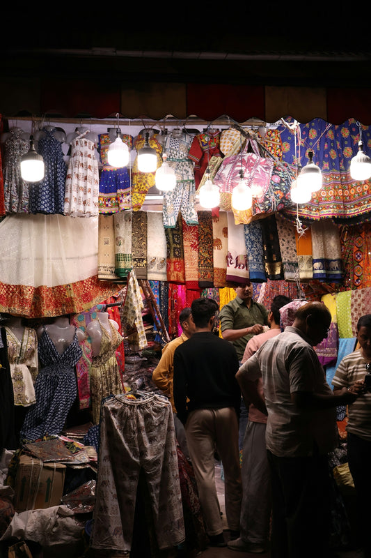 People browse colorful textiles at a busy market stall.